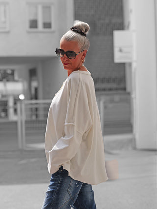 Ältere Frau trägt das OFF#DLY Sweat Elisa white mit lockerem Schnitt und langen Ärmeln, passend zu blauen Jeans. Ihr Look wird durch goldene Accessoires und große Sonnenbrille ergänzt.