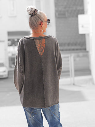 Person von hinten mit OFF#DLY Sweat Elisa anthrazit, lockerem Schnitt und Rückenausschnitt, kombiniert mit lässigen, farbgesprenkelten Jeans. Verleiht einen modernen, urbanen Look.