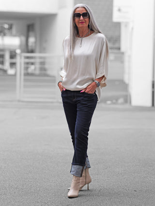 Ältere Frau trägt die OFF#DLY Dark Denim Luino, eine locker sitzende Jeans mit umgeschlagenem Saum und markanten Nähten, kombiniert mit beigen Stiefeletten und einem eleganten, lässigen Look.