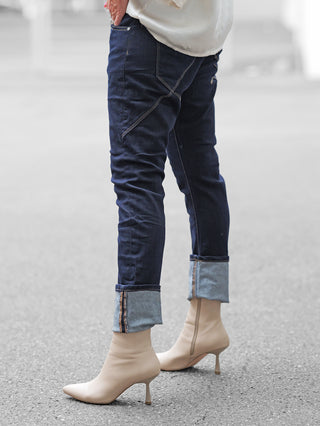 Eine Person trägt die OFF#DLY Dark Denim Luino mit hochgekrempelten Säumen und markanten Nähten, kombiniert mit cremefarbenen Ankle Boots und einem lockeren, weißen Oberteil.