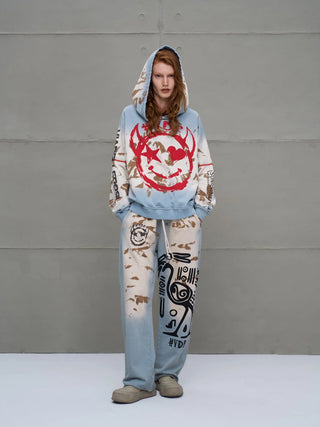 Junge Frau in #VDR Pant 18002 blue/beige, weit geschnittene, gebleichte Jogginghose mit abstrakten, schwarzen Motiven auf einem Bein und kleinem Smiley-Emblem auf dem anderen.