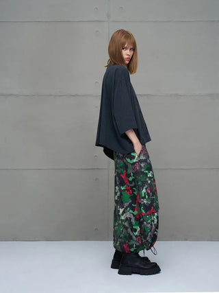 Junge Person seitlich im #VDR Tee 18007 black, einem oversized, schwarzen T-Shirt mit lockerem Schnitt und Halbarm, lässig über Cargohosen, Hände in den Taschen, vor Betonwand.