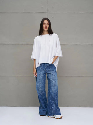 Junge Frau trägt #VDR Tee 18037 white, ein oversized, asymmetrisches T-Shirt mit halblangen Ärmeln, lockerem Schnitt und rosenförmigem Print auf der Rückseite, kombiniert mit blauen, weit geschnittenen Jeans.