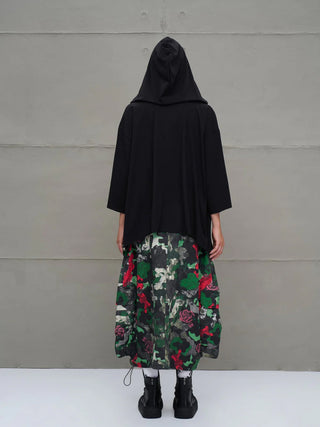 Person von hinten in lockerem #VDR Tee 18042 black, oversized mit Kapuze und asymmetrischem Schnitt. Kombiniert mit einem langen Camouflage-Rock und klobigen schwarzen Stiefeln.