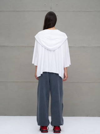 Person trägt #VDR Tee 18042 white, ein weißes, übergroßes, asymmetrisches Kapuzen-T-Shirt mit halblangen Ärmeln, über weiten, grauen Hosen und auffälligen roten Sneakers.