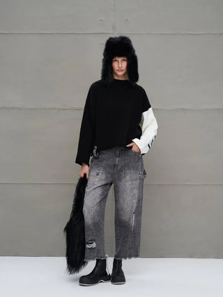 #VDR Strick 18068 black/white: Oversized Pullover mit einem weißen Ärmelpanel, Rundhalsausschnitt und Strick-Lettering-Details, getragen von einem Model mit grauen Denim-Hosen und schwarzen Boots.