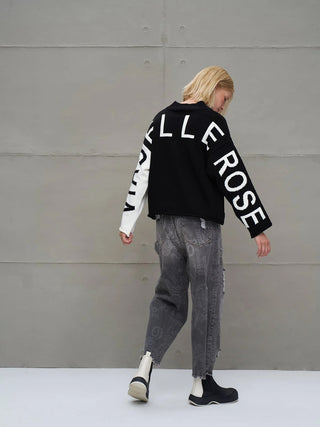 Eine Person trägt den #VDR Strick 18068 black/white, einen urbanen, übergroßen Strickpullover mit markanten weißen Buchstaben auf Rücken und Ärmeln, kombiniert mit kontrastfarbenen Ärmeln.