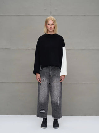 Person trägt #VDR Strick 18068 black /white, einen lässigen, kontrastfarbenen Pullover mit Rundhalsausschnitt und auffälligen Strick-Lettering-Details, kombiniert mit grauen Jeans und schwarzen Ankle Boots.