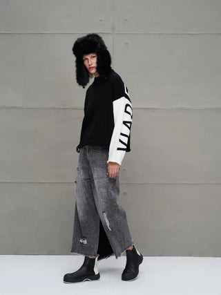 #VDR Strick 18068 black/white Pullover mit weißem Ärmel und auffälligen Blockbuchstaben, getragen von einem Model vor grauer Wand, kombiniert mit urbanem Streetwear-Look.