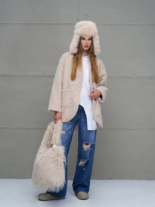 Junge Frau trägt #VDR Pan Hat beige, ein flauschiger Trapperhut mit Ohrenschützern und Nackenverschluss, passend zu ihrem flauschigen Outfit, darunter ein langes weißes Shirt und distressed Jeans.