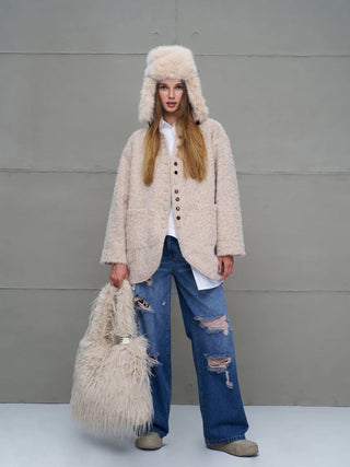 Junge Frau trägt #VDR Tasche PastelBag beige, eine große, flauschige Kunstfell-Tasche in Creme, passend zu ihrem Hut und Mantel, kombiniert mit lässigen, zerrissenen Jeans und neutralen Schuhen.