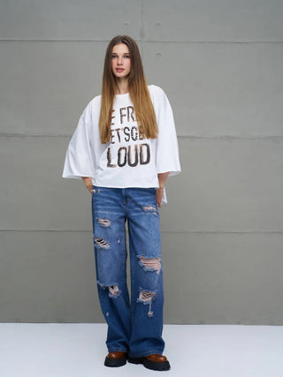 Junge Frau in #VDR Destroy Denim 18132 midblue Jeans mit weitem, distressed Schnitt und großen Rissen, kombiniert mit einem oversized T-Shirt und chunky Plattform-Schuhen, für einen lässigen Streetwear-Look.
