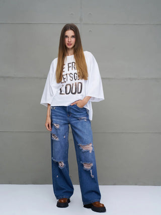 Junge Frau trägt #VDR Destroy Denim 18132 midblue: weite, stark zerstörte blaue Jeans mit hohem Bund und Back-Patch-Detail, kombiniert mit einem oversized weißen T-Shirt und klobigen zweifarbigen Platform-Schuhen.