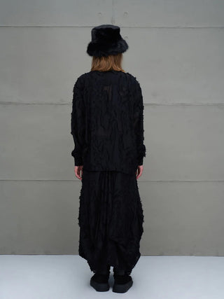 Das Model trägt das #VDR Shirt 18171 black, ein locker geschnittenes, semi-transparentes Oberteil mit Fransendetails und Mandarin-Kragen, kombiniert mit voluminösem, schwarzem Unterteil.