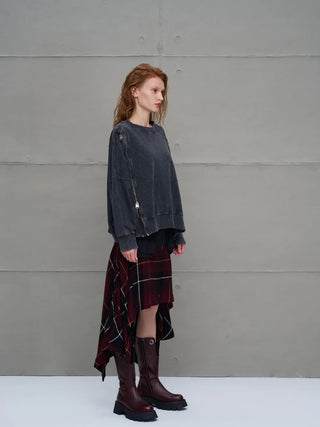 Junge Frau in #VDR Sweater 18005 anthrazit mit seitlichen Reißverschlüssen, oversized und lässig, in natürlicher Pose, kombiniert mit einem karierten Rock und burgunderfarbenen Stiefeln.