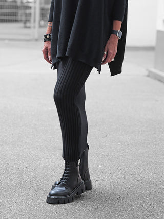 Unterkörper einer Person mit dem Rock Linda von OFF#DLY in Schwarz. Der Rock reicht bis zur Wade, hat ein feines Rippstrickdesign und wird mit klobigen schwarzen Schnürstiefeln kombiniert.