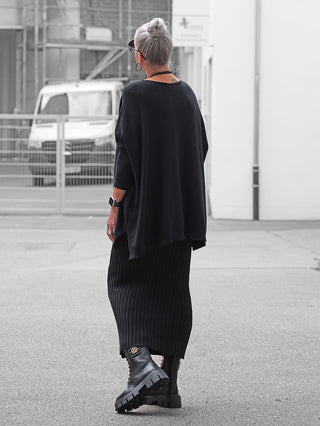 Ältere Frau trägt den OFF#DLY Pulli Olivia schwarz, einen oversized Pullover mit fließendem Fall und seitlichen Schlitzen, kombiniert mit einem langen Rock und klobigen Stiefeln.
