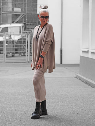Frau trägt den OFF#DLY Pulli Olivia taupe, ein oversized Strickset mit lockerem Pullover und passender Hose, kombiniert mit schwarzen Kampfstiefeln und Statement-Accessoires, vor urbanem Hintergrund.