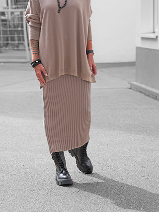Person trägt OFF#DLY Rock Linda taupe, ein geripptes, midilanges Strickdesign, kombiniert mit klobigen schwarzen Stiefeln. Der Rock ist elegant und komfortabel, mit elastischem Bund für perfekten Sitz.