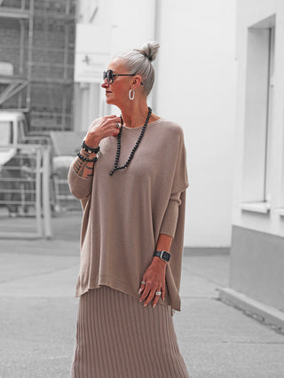 Silberhaarige Frau trägt den OFF#DLY Pulli Olivia taupe in Oversize mit weichem Fall, kombiniert mit einem langen Strickrock. Der Pullover hat seitliche Schlitze und bietet hohen Tragekomfort.
