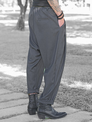 Person trägt OFF#DLY Baggy Pant Abby anthrazit, lockerer Schnitt mit Seitentaschen, kombiniert mit schwarzen Lederstiefeletten. Rechte Hand in der Hosentasche, tätowierter Unterarm mit Armbändern sichtbar.