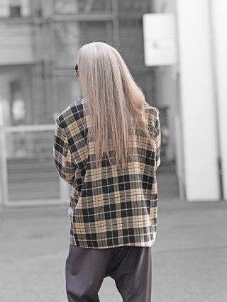 Person von hinten in urbaner Umgebung, trägt den Lumina Blazer black/white: Oversize-Karomuster mit Reverskragen, gepolsterten Schultern, Pattentaschen und einreihiger Knopfleiste, kombiniert mit dunklen Hosen.