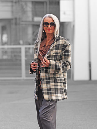 Frau mit silbernem Haar trägt den Lumina Blazer black/white, ein übergroßer Karoblazer mit Reverskragen, gepolsterten Schultern und Pattentaschen, kombiniert mit brauner Bluse und grauer Hose.