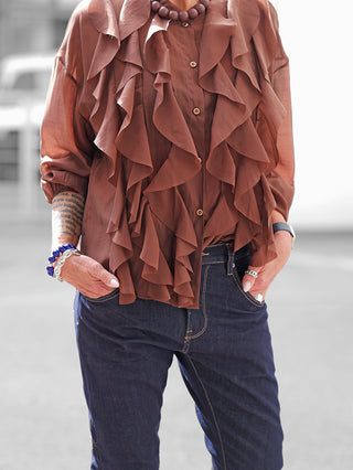 OFF#DLY Bluse Rita braun mit kaskadierenden Volants vorne, lockerer Schnitt, aus Lyocell-Polyester-Mix, getragen mit hochgekrempelten Ärmeln, dunklen Jeans und Accessoires, inklusive Armbanduhr.