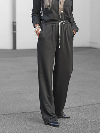 OFF#DLY Sweatpant Stilfs II black: Tragekomfort und Stil mit elastischem Bund und Seitentaschen, kombiniert mit spitz zulaufenden Schuhen, abgerundet durch silberne Armbänder und ein schwarzes Oberteil.