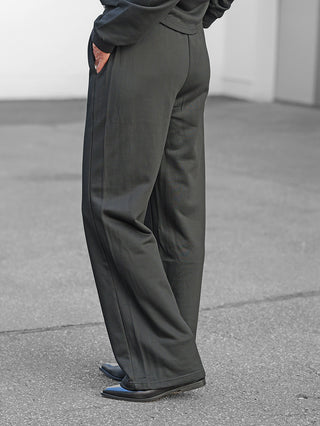 Person trägt OFF#DLY Sweatpant Stilfs II schwarz mit weitem Bein, kombiniert mit schwarzen, spitzen Schuhen; Hand in der Tasche, betont den sportlich-bequemen, stilvollen Look der Hose.