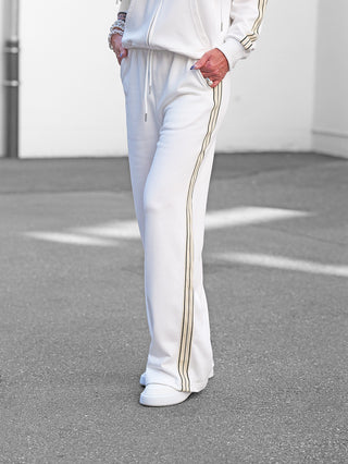 OFF#DLY Sweatpant Stilfs white: Eine Person trägt eine cremefarbene Jogginghose mit Kontraststreifen und weißen Sneakers. Hände in den Taschen, die Hose hat einen elastischen Bund und Seitentaschen.