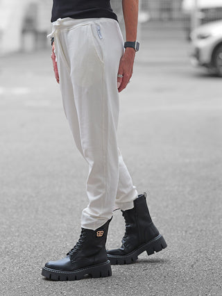Nuomeno Pant offwhite, schmal geschnittene Joggpant mit elastischem Bund und Kordelzug, getragen zu klobigen schwarzen Stiefeln. Die Hose bietet urbanen Komfort und Funktionalität für einen modernen Look.