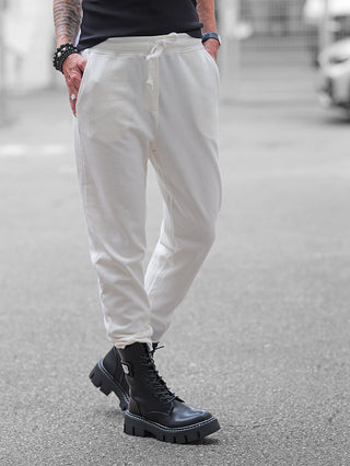 Nuomeno Pant offwhite: Jogger-Hose mit schmalem Schnitt, elastischem Bund und Kordelzug, getragen mit klobigen schwarzen Stiefeln. Sichtbar sind Tätowierungen und Schmuck an den Armen.