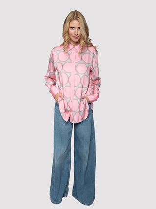 Frau trägt Emily Damenbluse rose dots, eine locker geschnittene, rosa Bluse mit Maxi-Punktemuster auf Viskose-Satin, kombiniert mit hoch taillierten, weiten blauen Jeans.