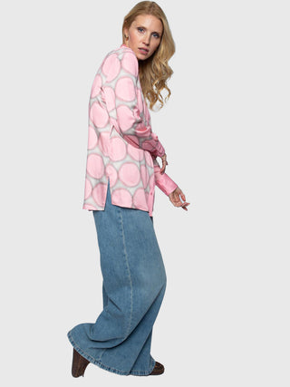 Frau trägt die Emily Damenbluse rose dots, eine lockere rosa Bluse mit Maxi-Dot-Print und durchgehender Knopfleiste, kombiniert mit weiten, hochtaillierten blauen Jeans und braunen Schuhen.