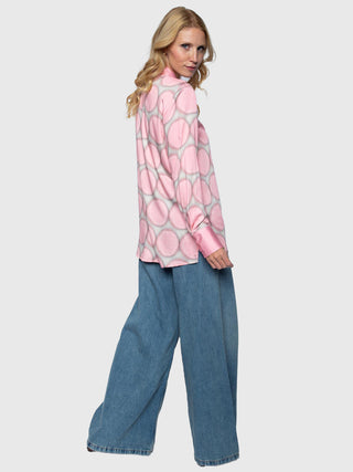 Modell trägt die Emily Damenbluse rose dots aus pastellrosa Viskose-Satin mit großen grauweiß versetzten Punkten, kombiniert mit weit geschnittenen blauen Palazzo-Jeans für einen modischen, lässigen Look.