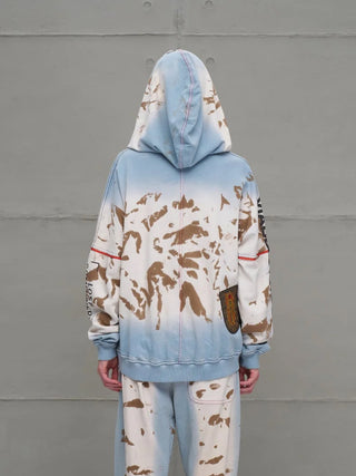 Rückansicht einer Person im #VDR Sweatshirt 18000 blue/beige mit Kapuze, unregelmäßigen Spritzflecken und einem kleinen gestickten Patch, betont den urbanen Streetstyle.