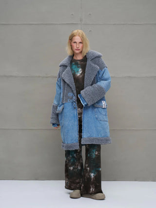 Junge Frau trägt #VDR Mantel 18077 blue, einen oversized Denim-Mantel mit grauem Faux-Fur an Kragen, Ärmeln und Saum, über einem dunklen, weiten Tie-Dye-Ensemble.