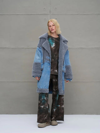 Eine Frau trägt den #VDR Mantel 18077 blue, einen übergroßen Denim-Mantel mit breitem Reverskragen, grauem Sherpa-Besatz und Bindegürtel, der urbanen Stil mit luxuriösem Flair vereint.