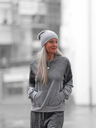 Frau trägt den OFF#DLY Jogginganzug BlingBling grey mit Strass-Details, bestehend aus grauem Sweatshirt und Sweatpants. Der Anzug bietet lässigen Komfort und Glamour bei leichtem Regen.