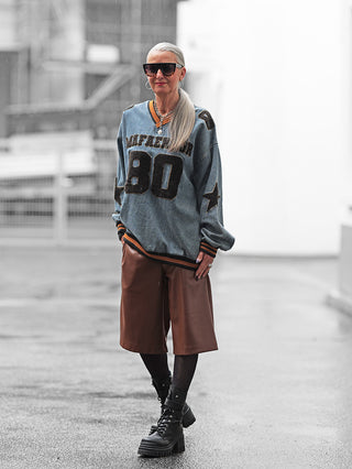 Eine Frau trägt das OFF#DLY Denimshirt Ariane blue mit 80-Flock-Print und Sternmotiven auf den Ärmeln, kombiniert mit braunen Leder-Shorts und schwarzen Stiefeln.