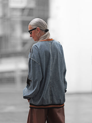 Person von hinten, urbanes Setting, trägt das OFF#DLY Denimshirt Ariane blue mit oversized Schnitt und Streifendetail am Saum. Kombiniert mit schwarzen Cat-Eye-Sonnenbrillen und großen, silbernen Ohrringen.