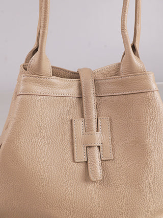 Nahaufnahme der OFF#DLY Leder Tasche beige mit Korpus aus beigefarbenem, kieselgenarbtem Leder, zwei Schulterriemen und einem zentralen Lederriemen, der durch eine H-förmige Schnalle als Verschluss geführt wird.