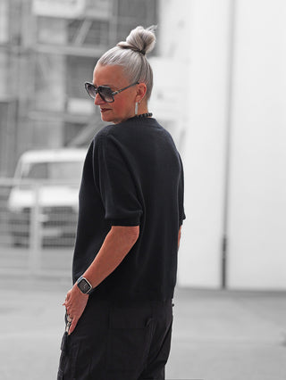 Ältere Frau trägt den OFF#DLY Pulli Tina black, ein schlichtes, modern geschnittenes Basic mit kurzen Ärmeln, ideal für einen eleganten urbanen Look, kombiniert mit schwarzen Cargohosen.