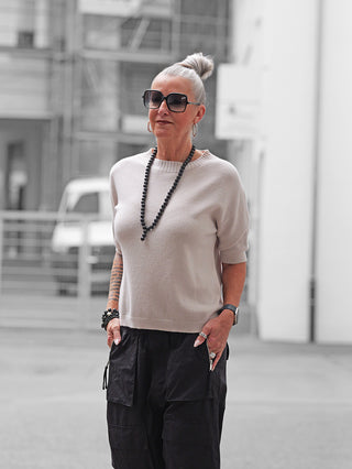 Ältere Frau trägt den OFF#DLY Pulli Tina stone, einen kurzärmeligen, schmal geschnittenen Pullover, kombiniert mit schwarzen Cargo-Hosen und Accessoires, für einen modernen, vielseitigen City-Look.