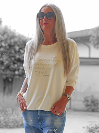 Ältere Frau im Garten trägt den OFF#DLY Sweater Beauty mit lässigem Schnitt und Statement-Print. Kombiniert mit Jeans, zeigt sie einen modernen, komfortablen Look.