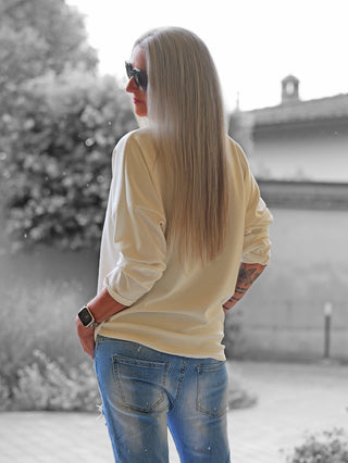 Eine Person trägt den OFF#DLY Sweater Beauty mit lockerem Schnitt und Statement-Print, kombiniert mit blauen Jeans und einer auffälligen Uhr im Freien.