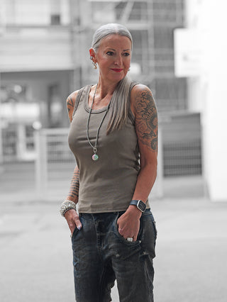 Ältere Frau in urbaner Umgebung trägt das OFF#DLY Top Neve taupe, ein lässiges Baumwoll-Top mit Smiley-Patch, kombiniert mit lockeren Jeans und auffälligen Accessoires.