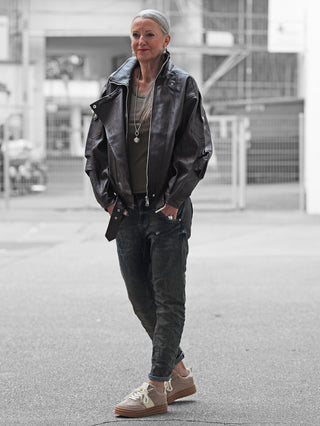 Ältere Frau trägt die OFF#DLY Biker Jacke coffee, eine oversized Lederjacke mit Revers und Zipper-Details, kombiniert mit dunkel gekleidetem urbanem Stil auf einer Straße.