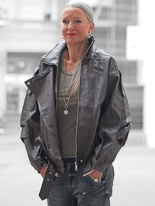 Ältere Frau trägt die OFF#DLY Biker Jacke coffee, eine oversized Lederjacke mit markanten Zipper-Details und extragroßen Revers, kombiniert mit Jeans in urbaner Umgebung.
